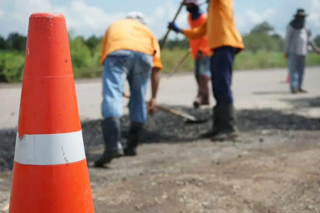 Road workers repairing asphalt with a traffic cone in the foreground