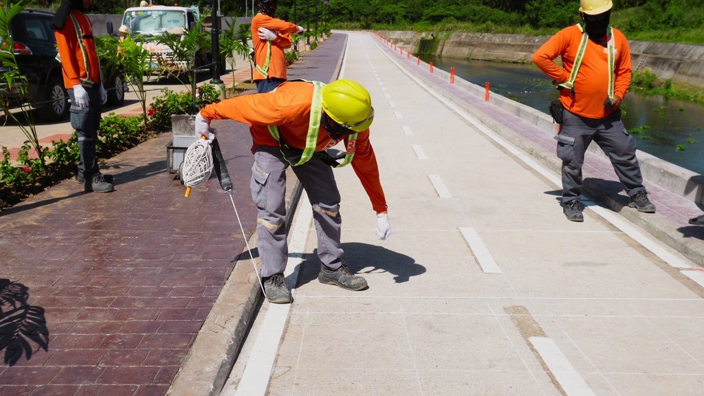 Road crew in orange safety vests and hard hats marking lane lines on a concrete bike lane using a pre-marking chalk line