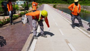 Road crew in orange safety vests and hard hats marking lane lines on a concrete bike lane using a pre-marking chalk line