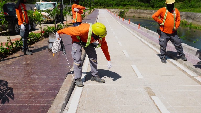 Road crew in orange safety vests and hard hats marking lane lines on a concrete bike lane using a pre-marking chalk line